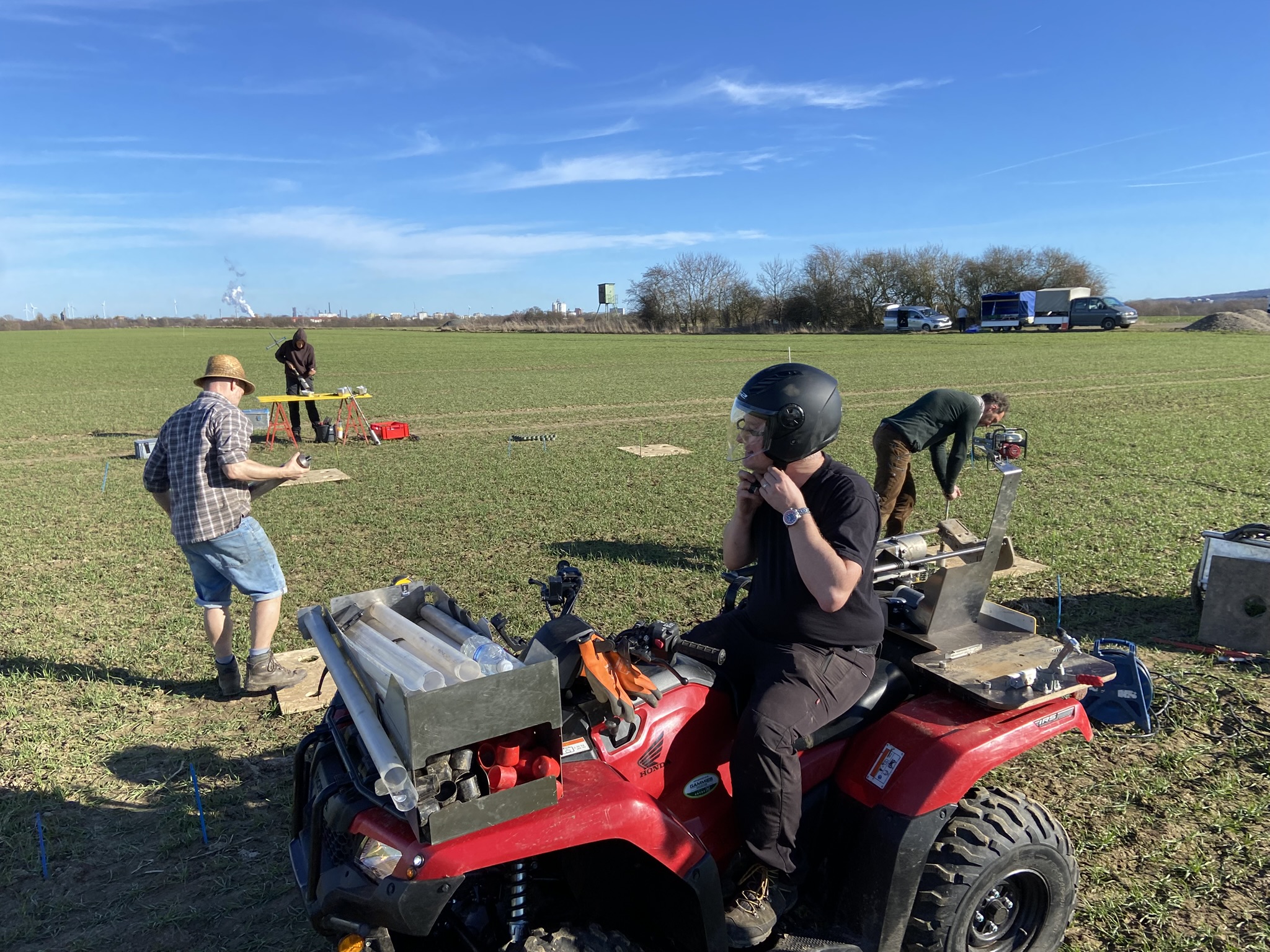 Researcher on an ATV with sampling tubes in a field.
