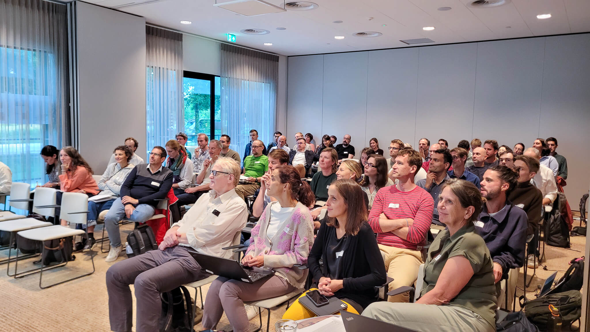 A large group of people seated in chairs, engaged in discussion within a spacious room.