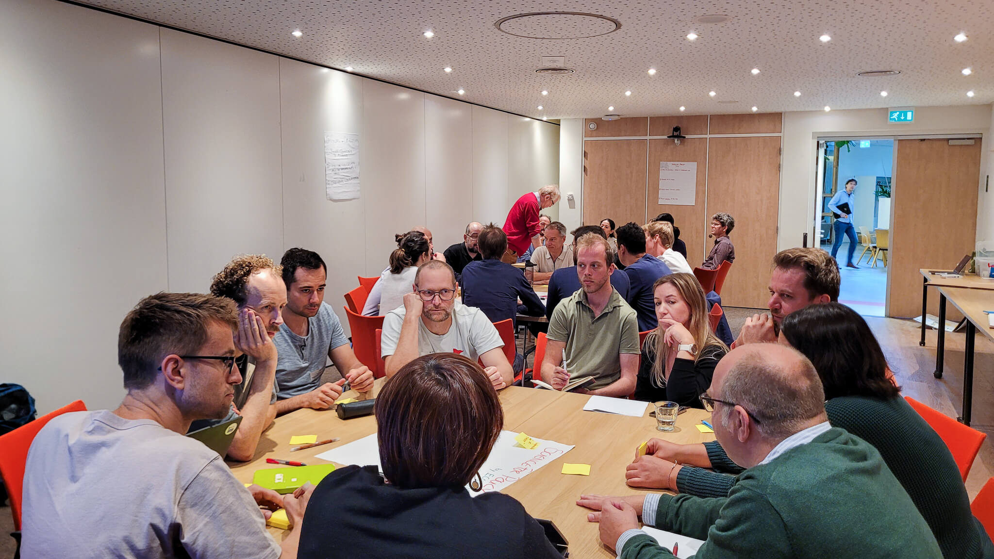 A group of diverse individuals seated around a table in a meeting room, engaged in discussion and collaboration.